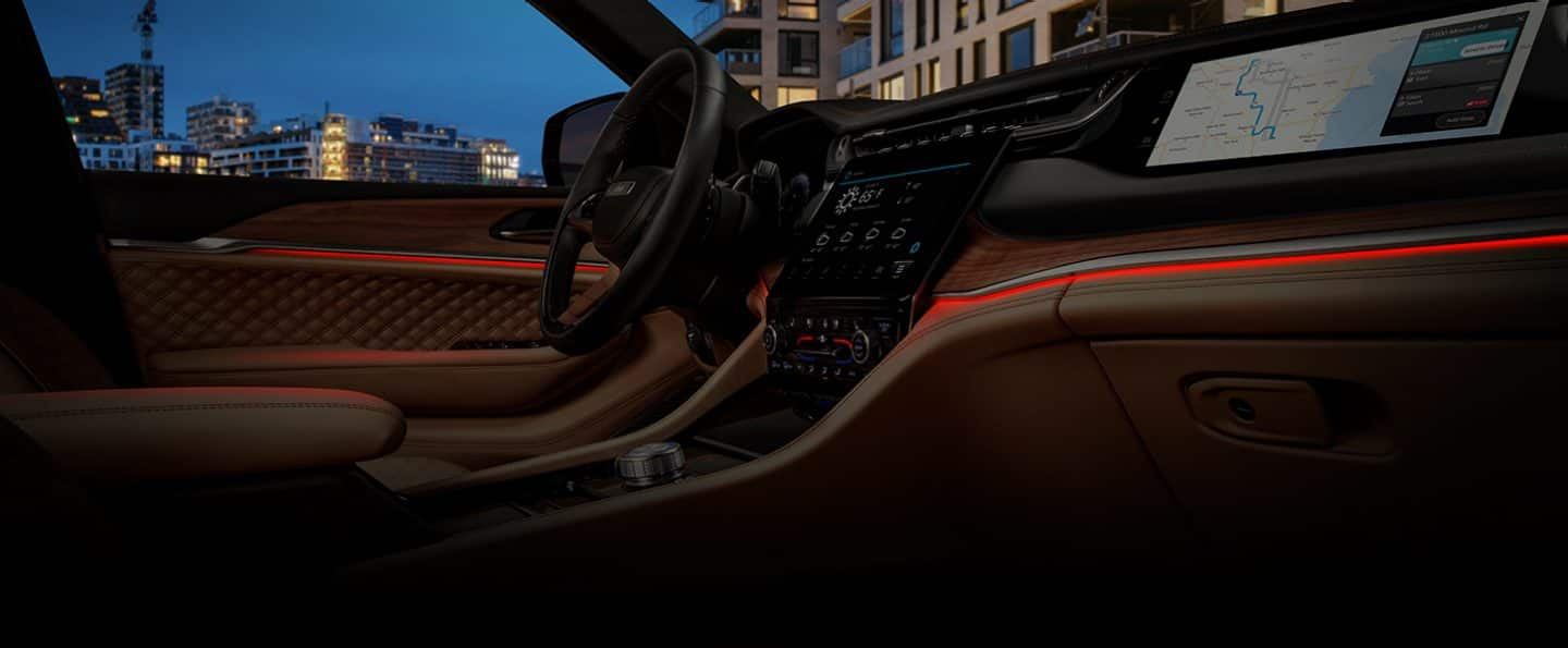 The front seat area of the 2024 Jeep Grand Cherokee Summit Reserve with red LED linear lighting woven through the door panels and dash.