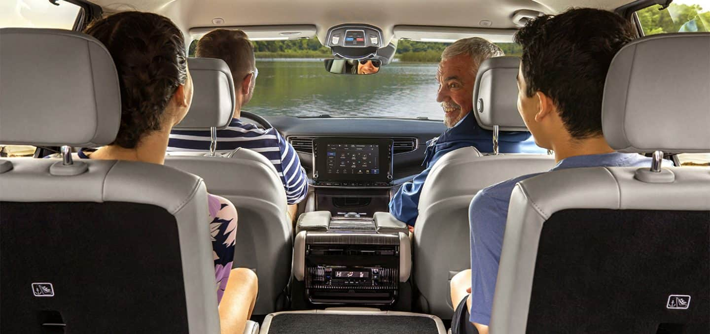 Display The interior of a 2023 Wagoneer Series III with a family of four on board and a view of the water through the windshield.