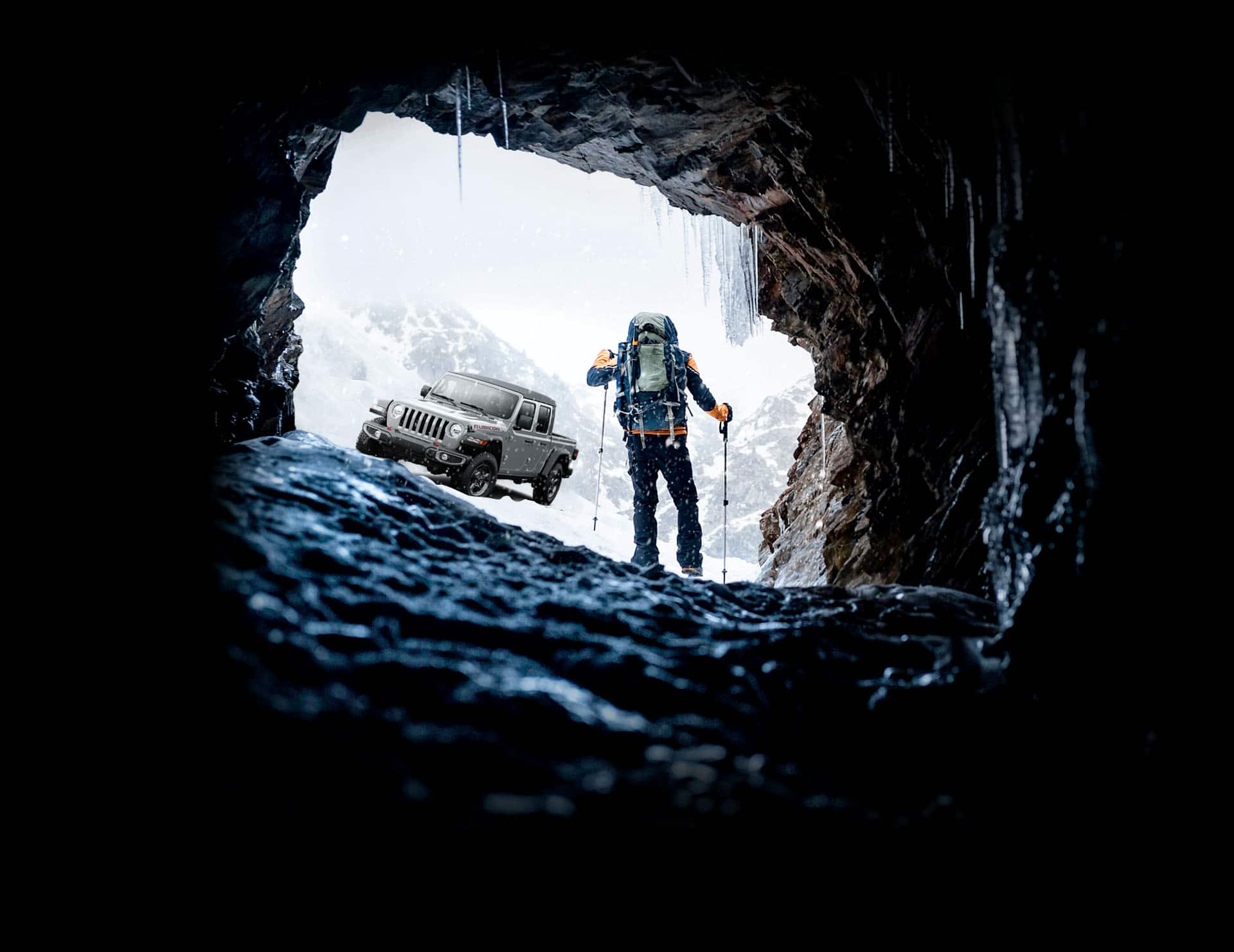 The 2023 Jeep Gladiator Rubicon as a mountain climber walks toward it, emerging from a frigid cavern in the snow-covered mountains.