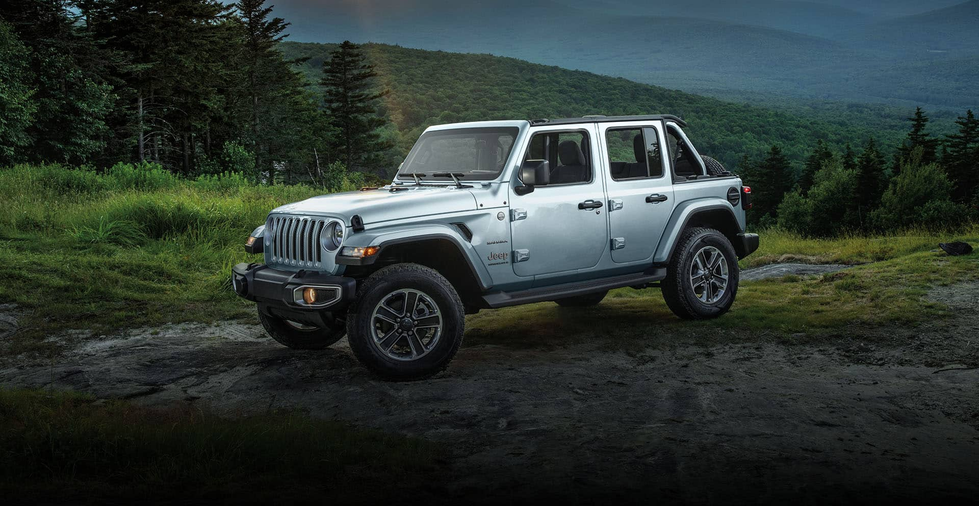 The 2023 Jeep Wrangler Sahara parked off-road on a patch of bare earth surrounded by grass and trees.