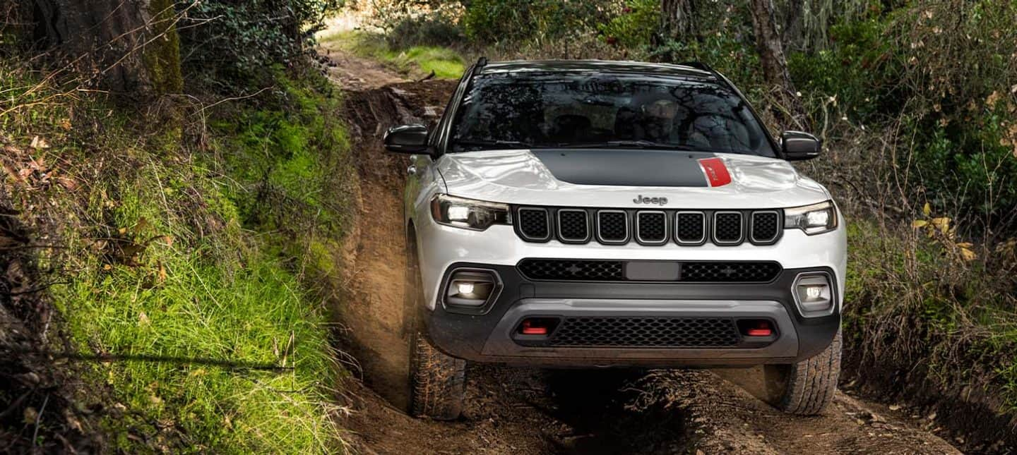 A head-on angle of a 2024 Jeep Compass Trailhawk being driven off-road through a narrow trail with thick growth on both sides. 