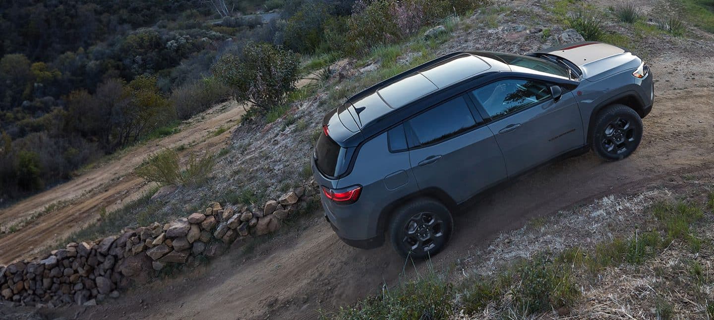 A 2024 Jeep Compass Trailhawk ascending a steep dirt road beside a stone fence.