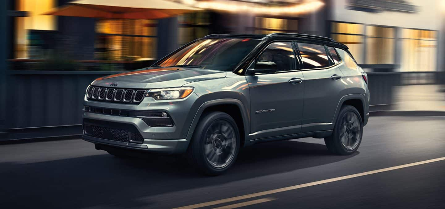 Display A 2024 Jeep Compass High Altitude being driven on a city street at night with the background blurred to indicate the vehicle is in motion.