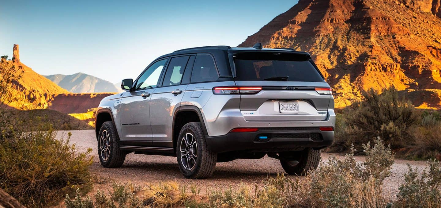 Display A silver 2024 Jeep Grand Cherokee Trailhawk 4xe parked on a clearing off-road, surrounded by hills of stone.