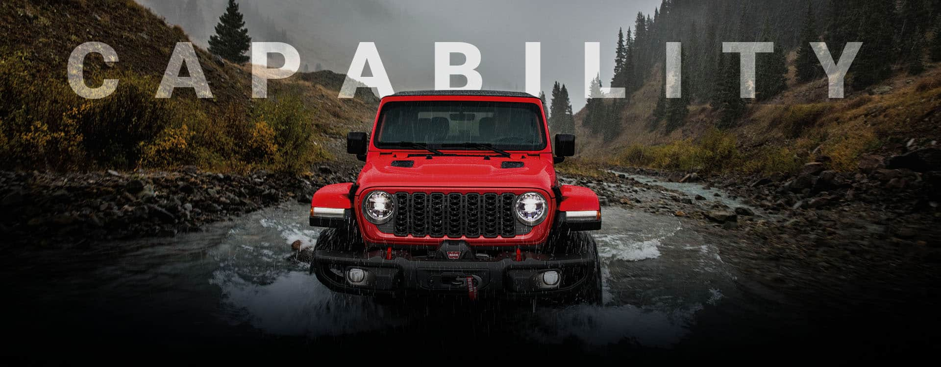 A front angle of a red 2024 Jeep Wrangler Rubicon being driven through a stream, following its path. Capability.